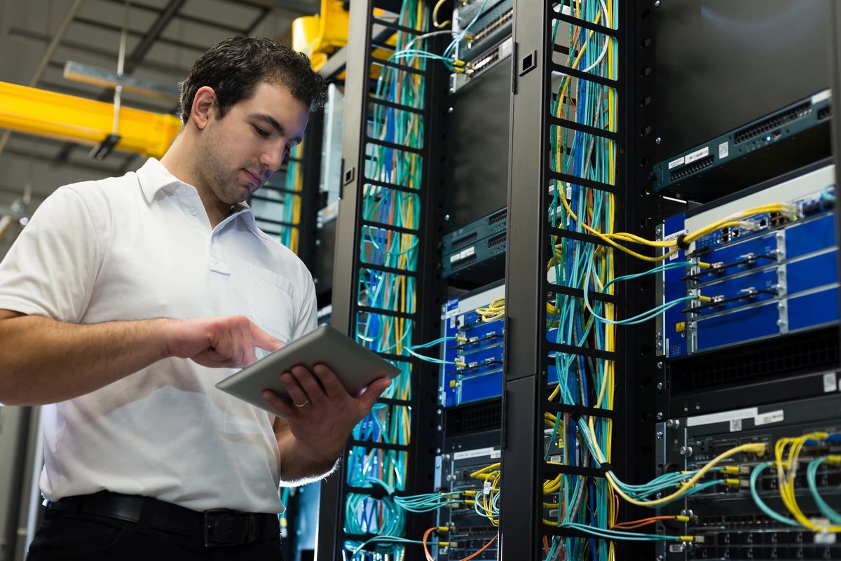 Technician using a tablet in a server room with network cables.