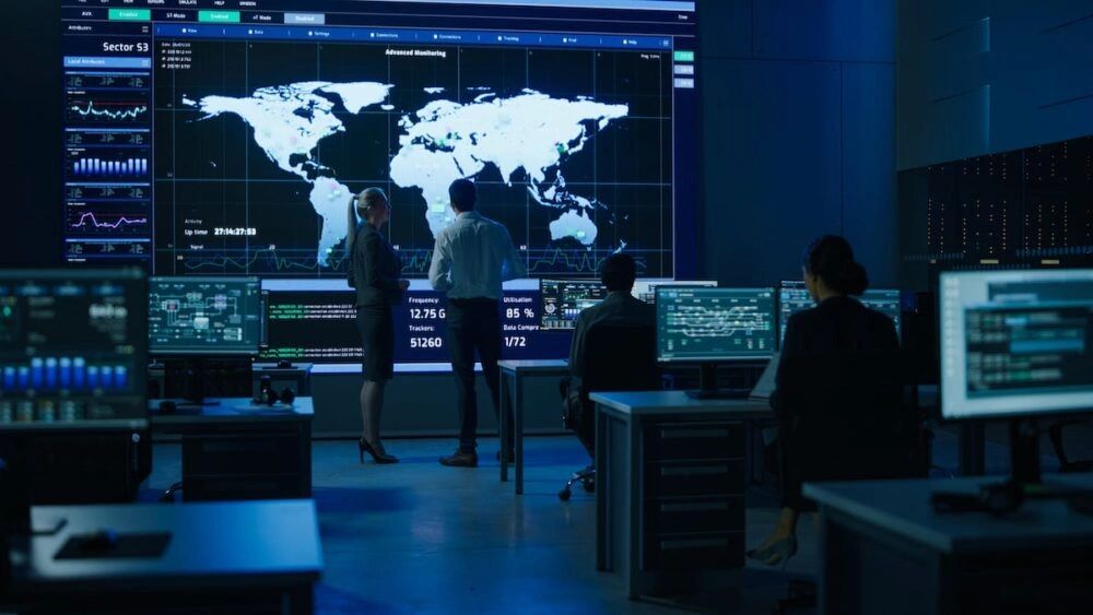 Team analyzing global data on large digital screens in a modern control room.